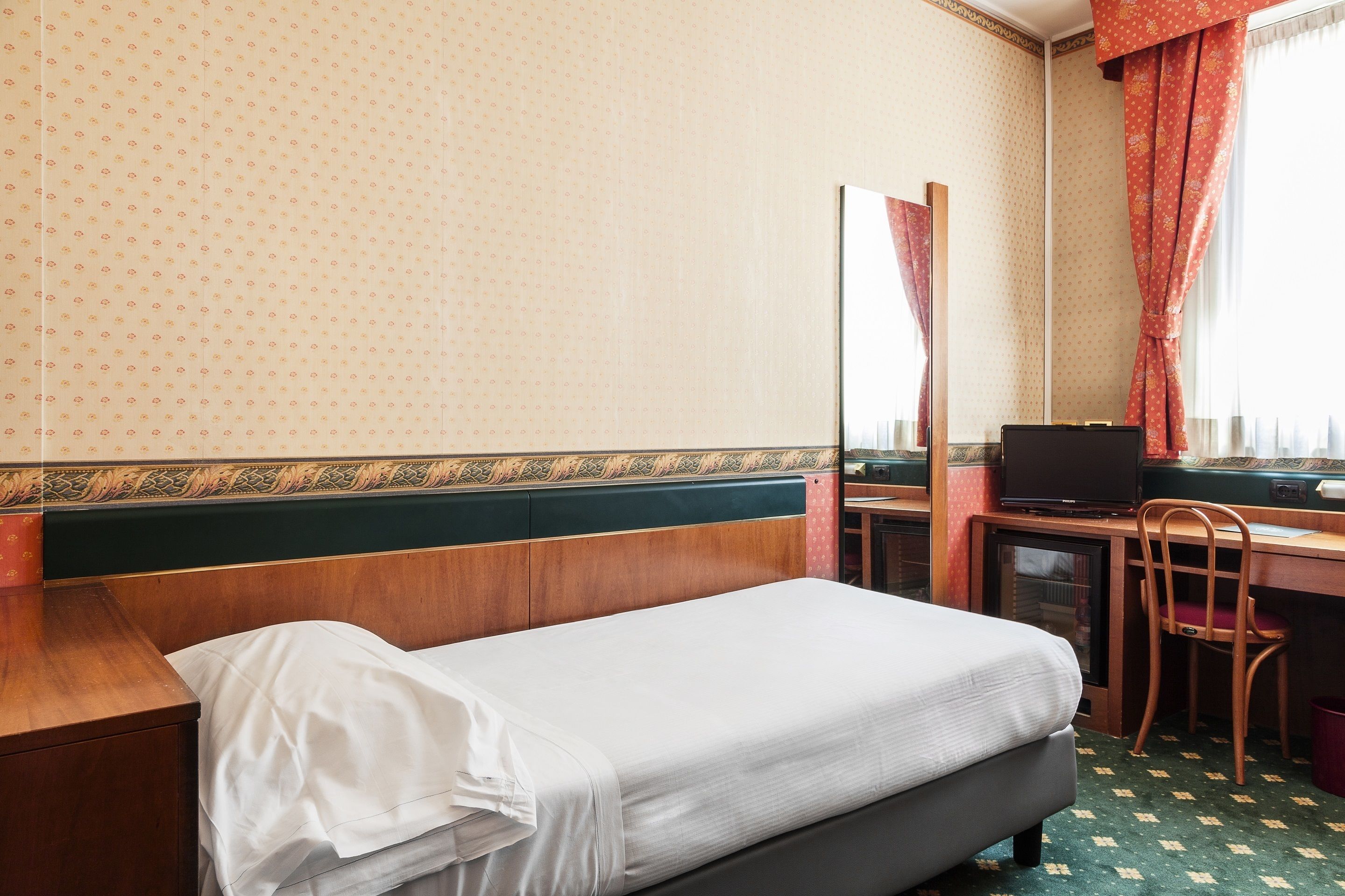 A hotel room with a single bed, a desk with a chair, a television, and a small cabinet.