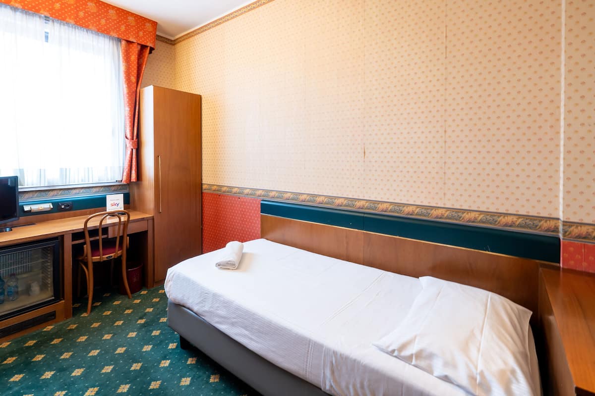 A hotel room with a single bed, a desk with a computer, a chair, and a wardrobe.