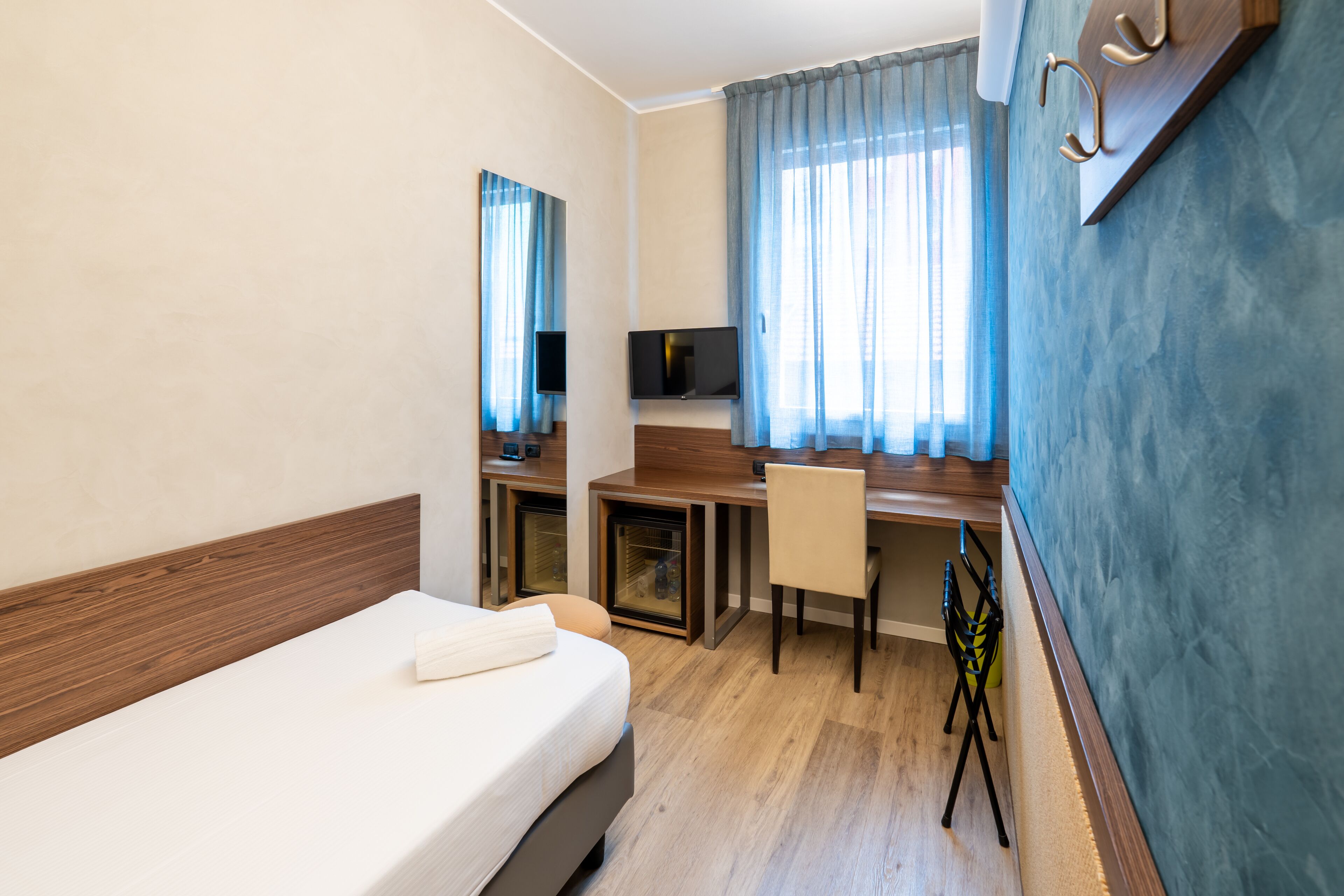 A hotel room with a bed, a desk, a chair, a TV, and a window with curtains.