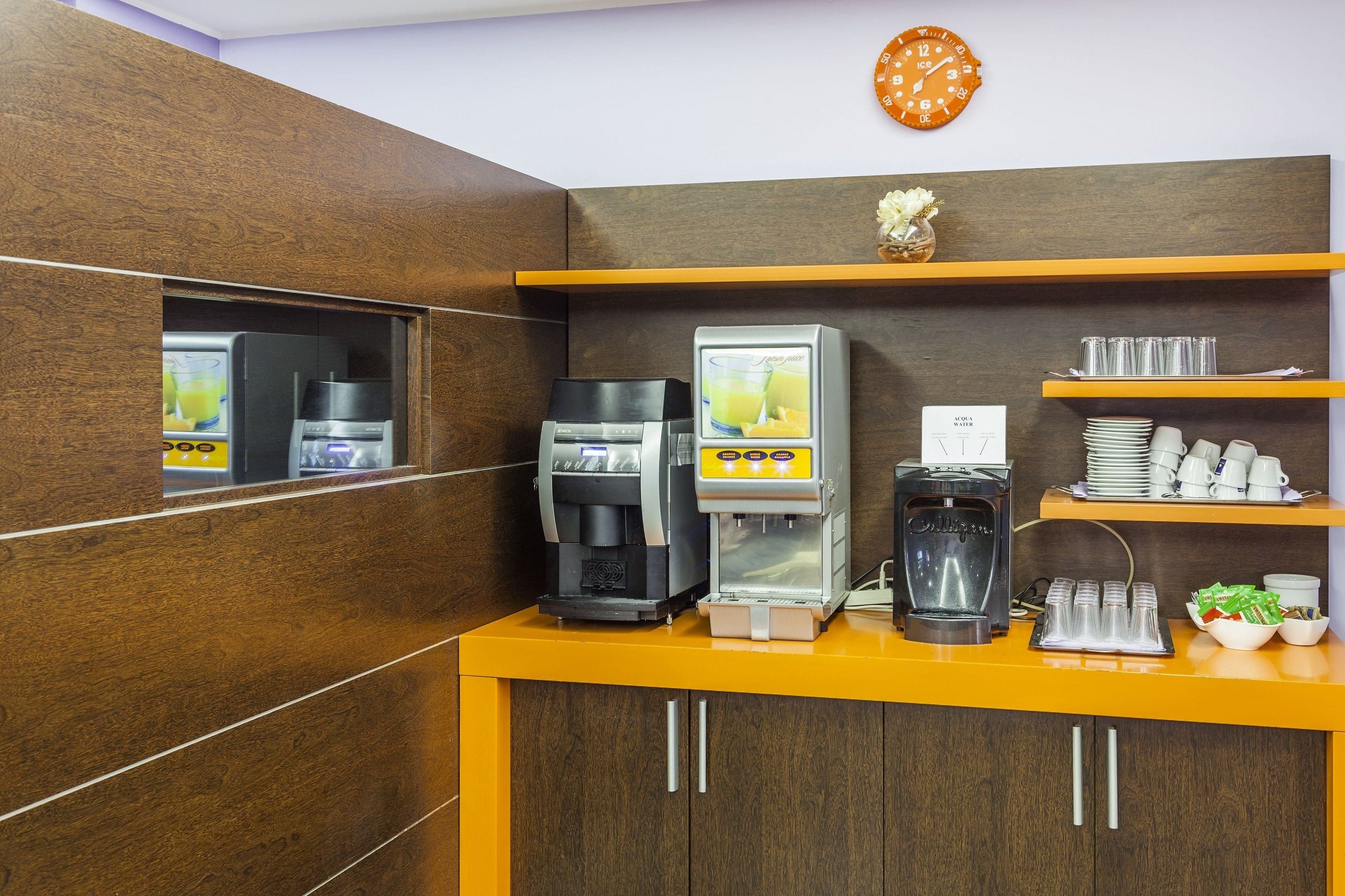 Una estación de café con varias máquinas de café, un reloj y un estante con tazas y platos.