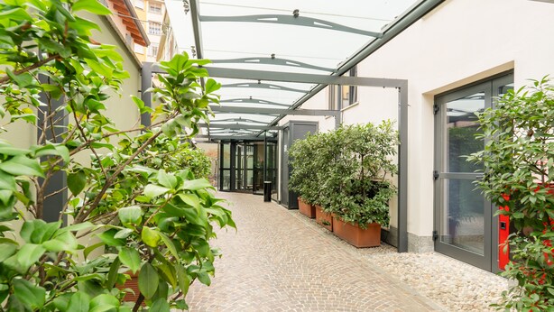 A covered outdoor corridor with potted plants, a cobblestone path, and a modern building facade. - Hotel Des Etrangers (Milan)