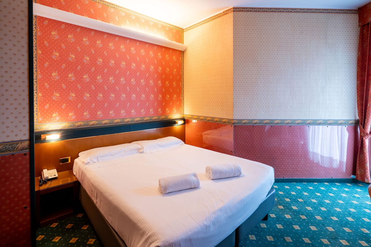 A hotel room with a bed, a nightstand, a telephone, and a window with curtains.