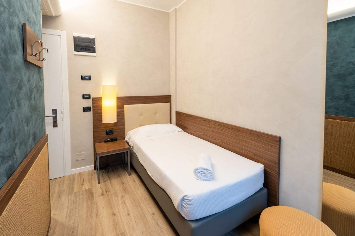 A hotel room with a single bed, bedside table, lamp, and a small seating area.