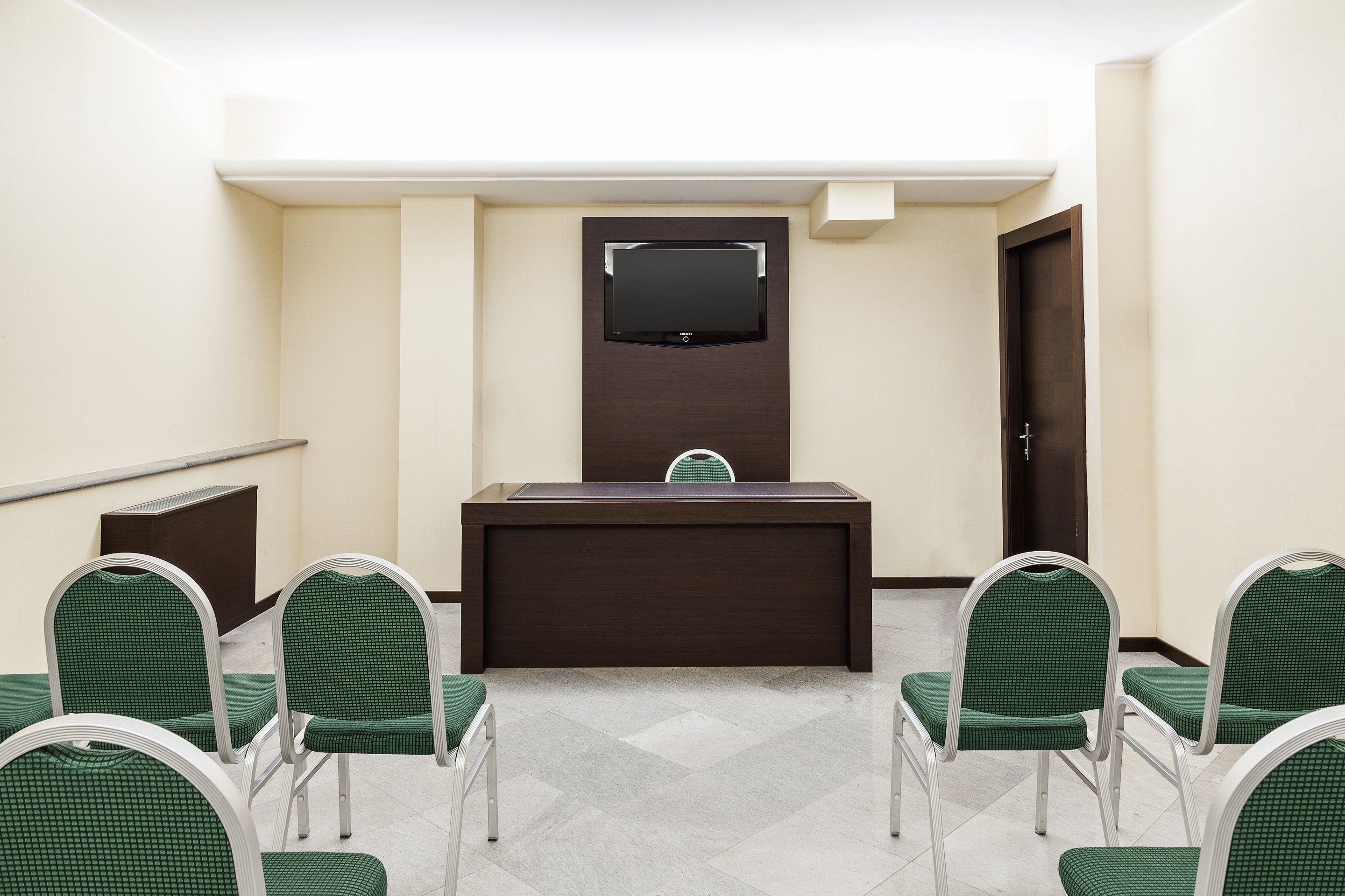 Une salle de conférence équipée d’un comptoir d’accueil, d’un téléviseur à écran plat et de fauteuils à revêtement vert.