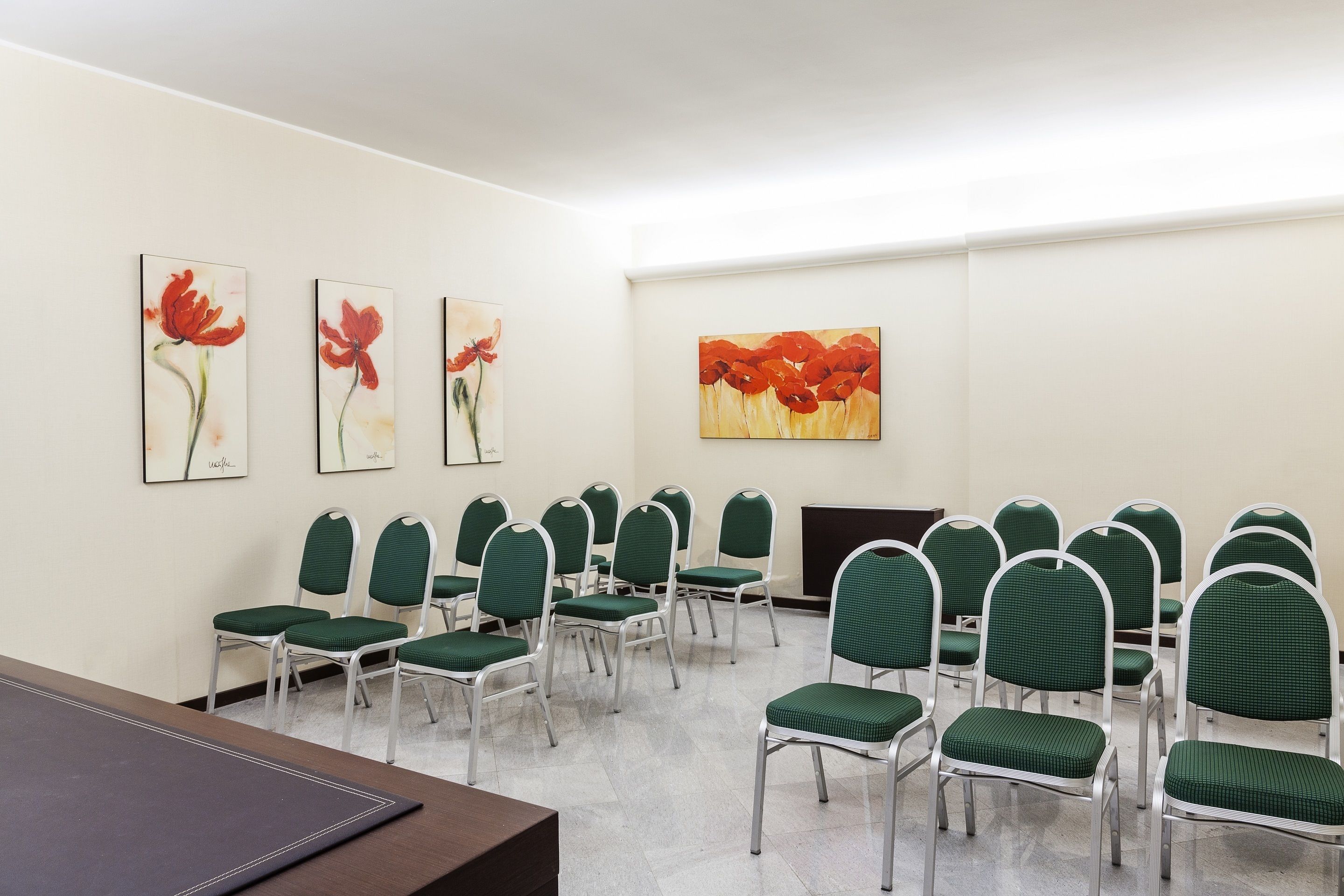 A conference room with green chairs and a large table. There are three paintings on the wall.