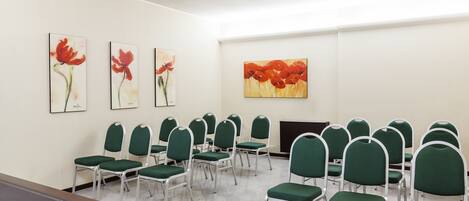A conference room with green chairs and a large table. There are three paintings on the wall.
