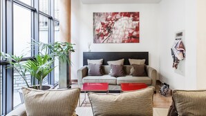 A modern living room with a sofa, two red side tables, and a large abstract painting on the wall. - Hotel Des Etrangers (Milan)