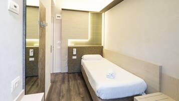 Una habitación de hotel pequeña y moderna con una cama individual, una mesita de noche, un espejo y una ventana.