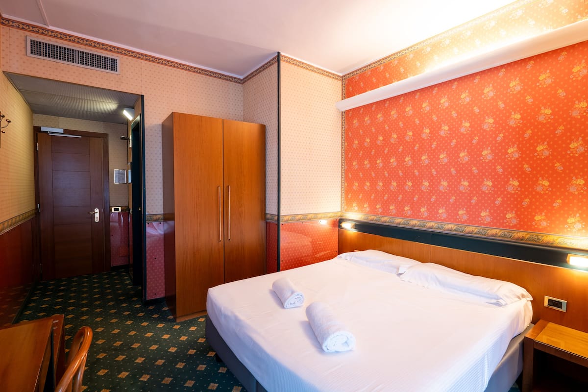 A hotel room with a bed, a wardrobe, a desk, and a chair.