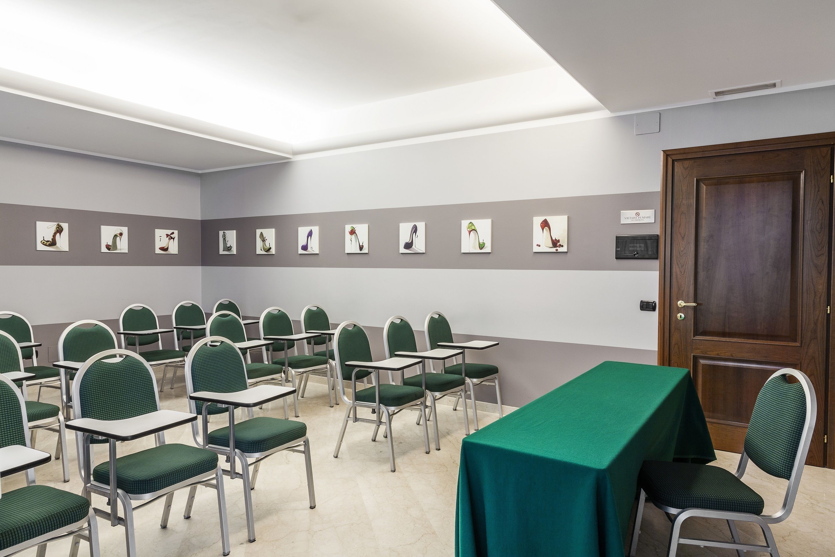 Une salle de conférence avec des chaises et des tables vertes, une porte en bois et des œuvres d’art accrochées aux murs.