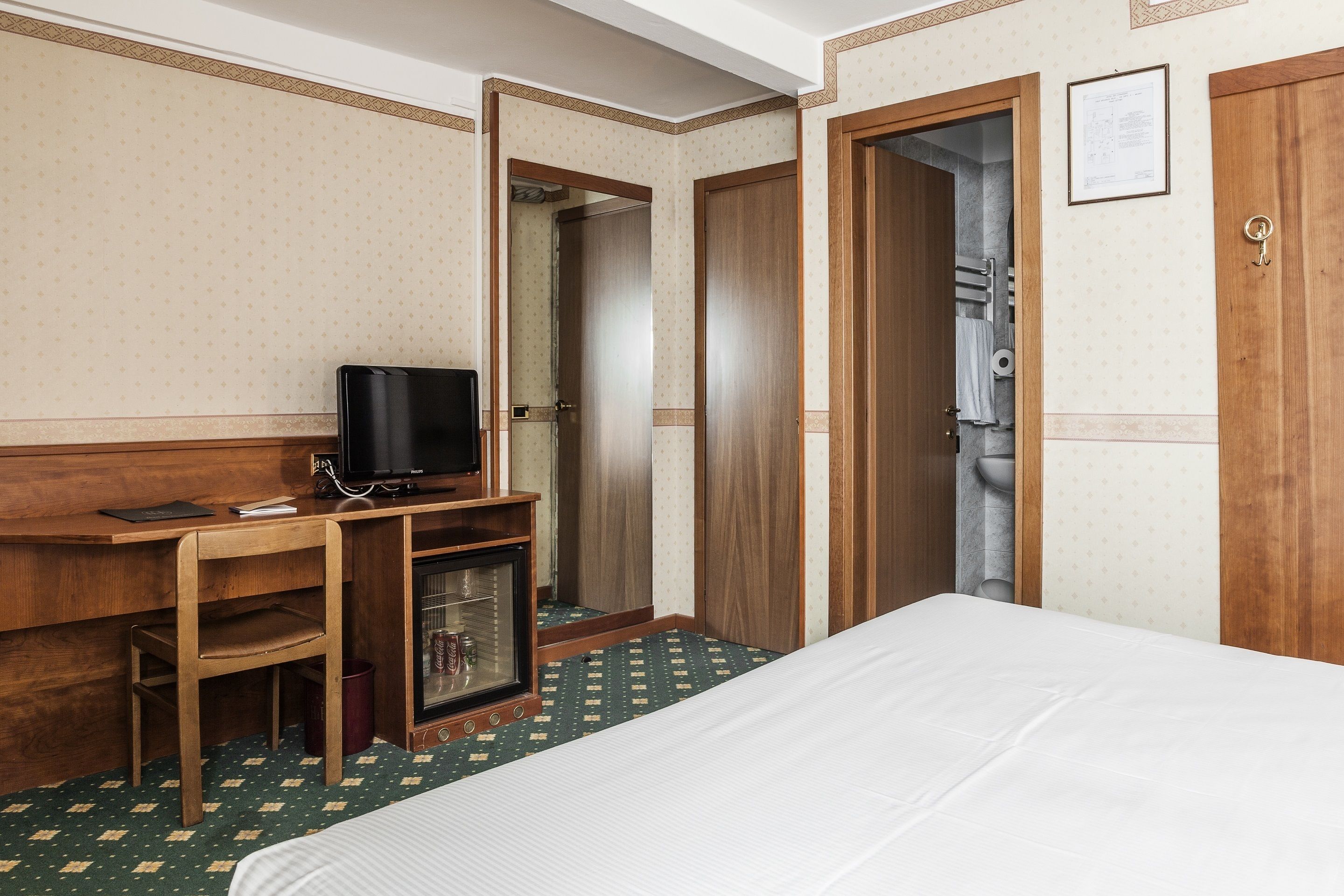 A hotel room with a bed, a desk with a television, a small cabinet, and a wardrobe.