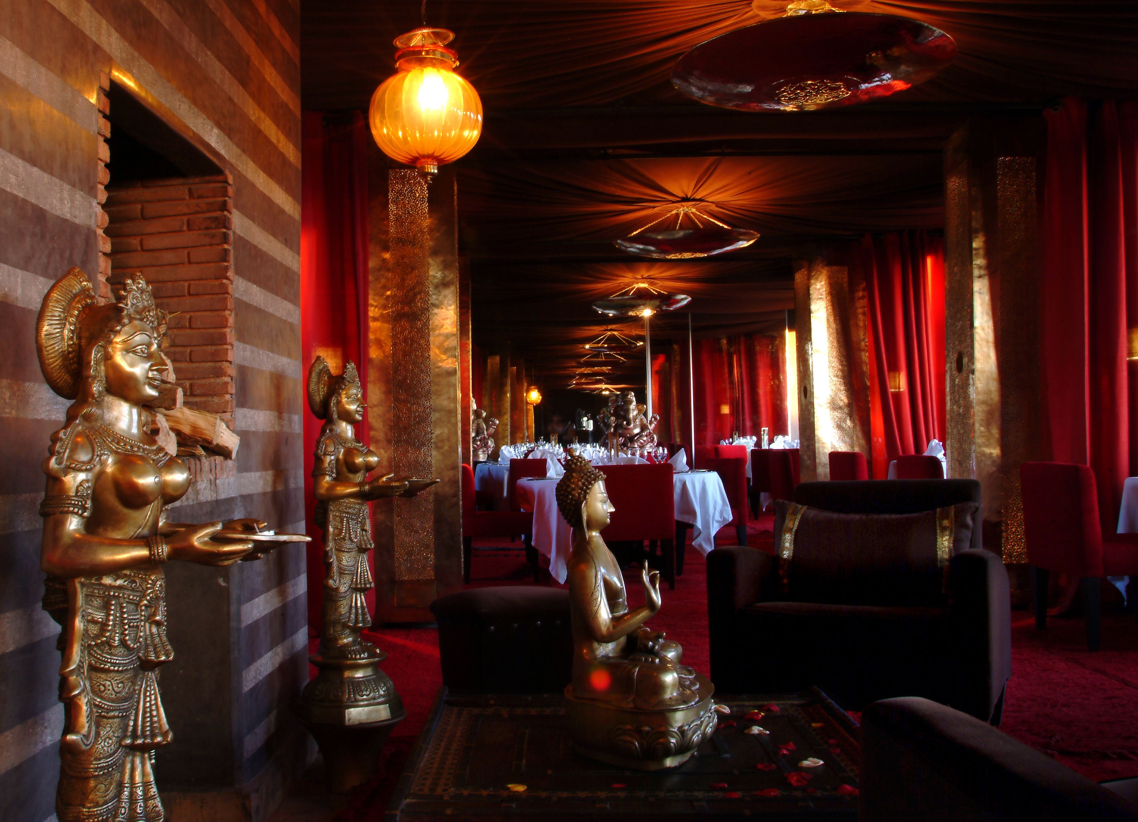 Un restaurante con un largo pasillo, cortinas rojas y una estatua de Buda.
