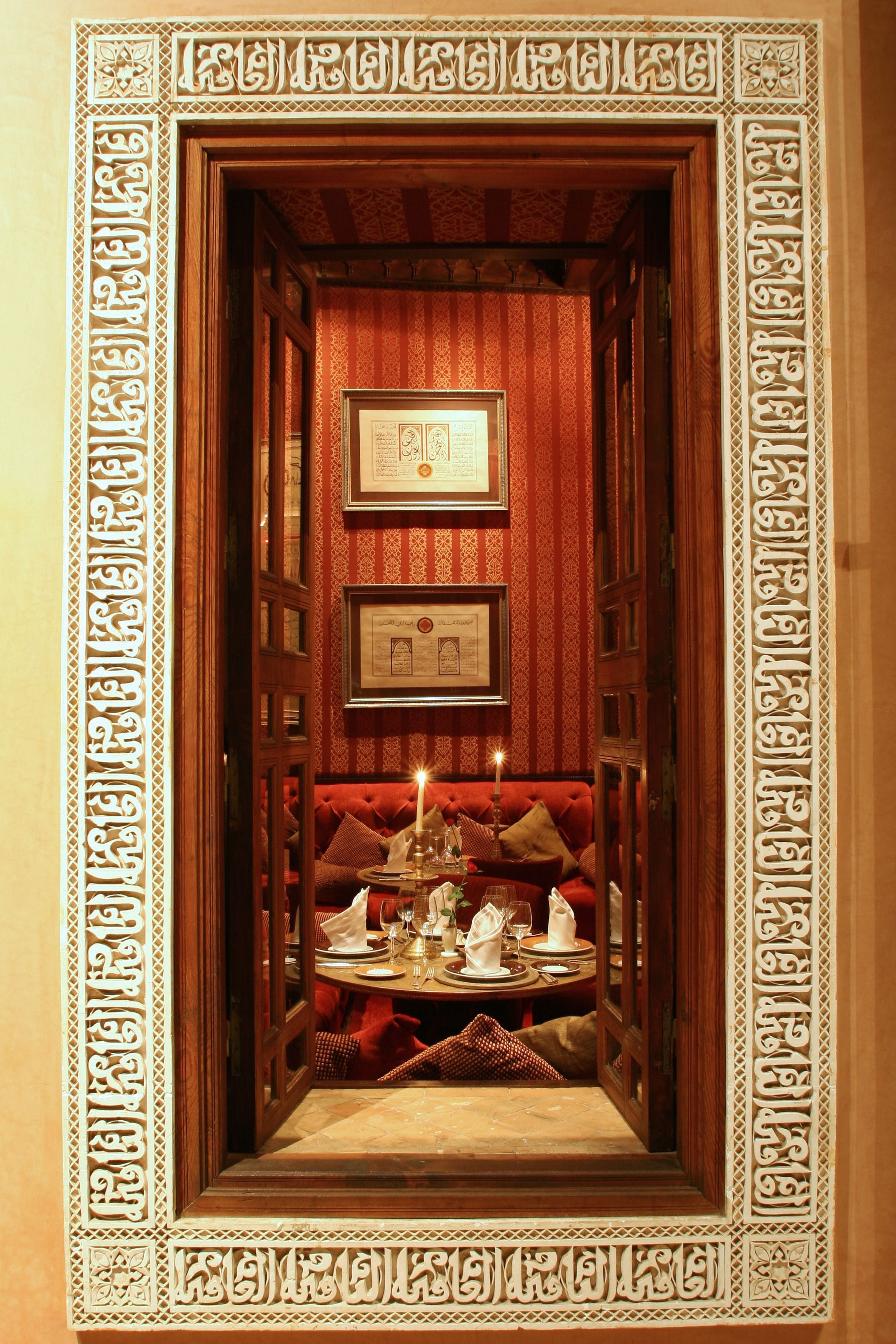 Un pasillo estrecho con puertas y paredes de madera ornamentada, que conduce a un área de estar con una mesa dispuesta para comer.