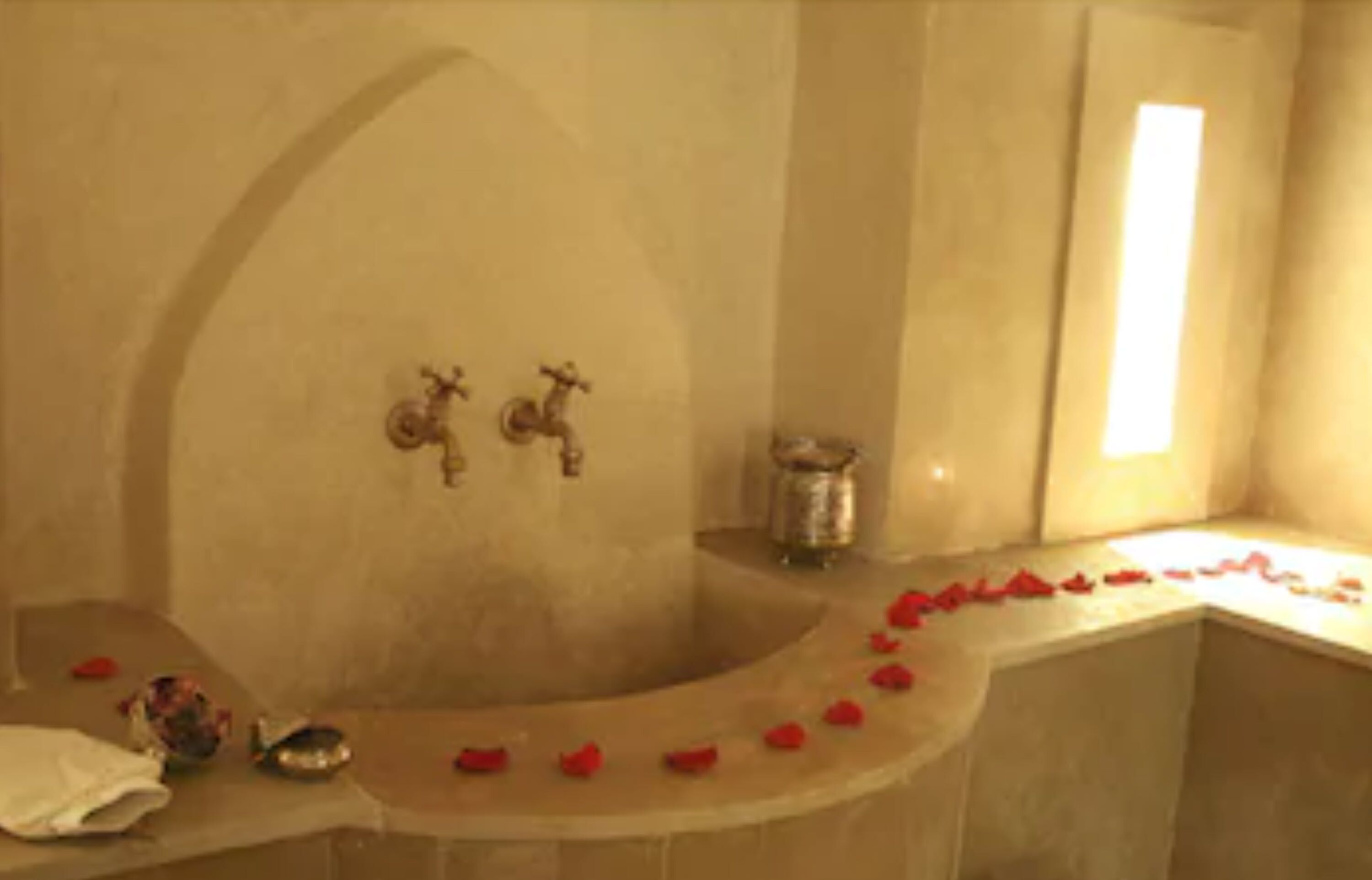 A bathtub with a curved edge, a small shelf with a decorative item, and a wall-mounted faucet.