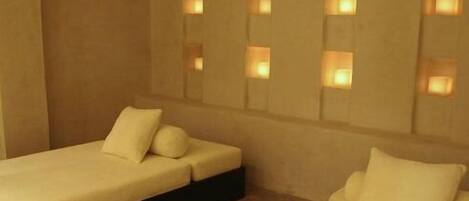 A room with two beds, each with a pillow and a headboard. There are wall-mounted lights above the beds.