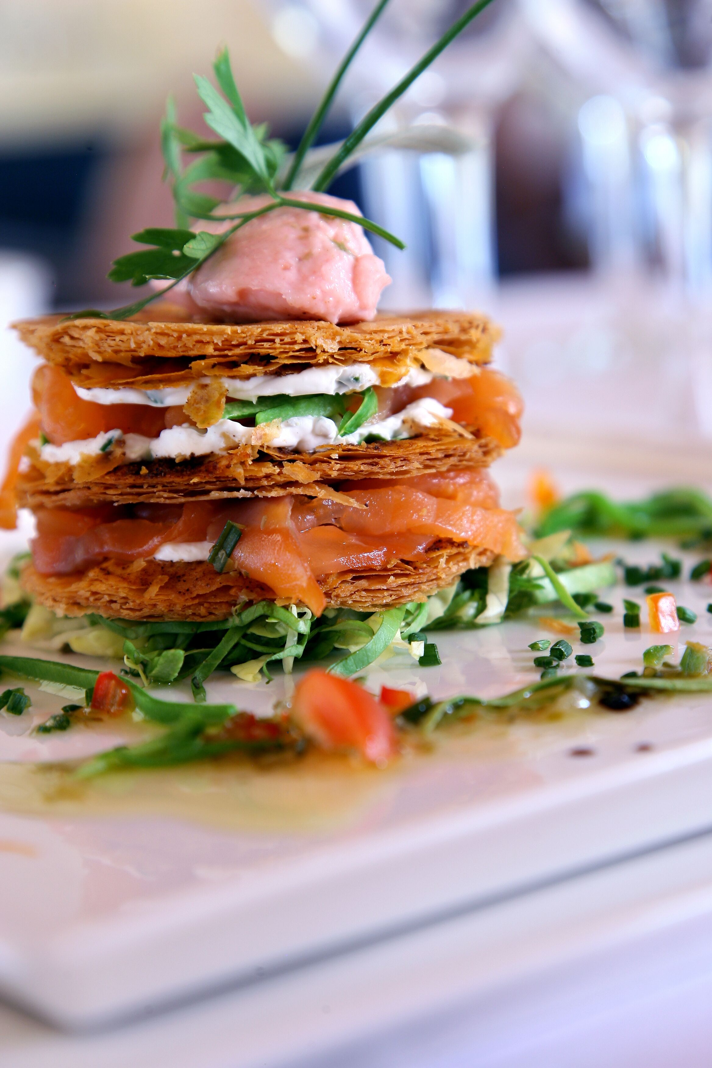 A layered sandwich with smoked salmon, cream cheese, and greens, garnished with a sprig of parsley.