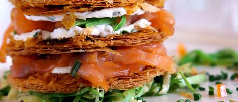 A layered sandwich with smoked salmon, cream cheese, and greens, garnished with a sprig of parsley.