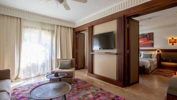 Una habitación de hotel con una cama grande, un televisor montado en la pared, un ventilador de techo y vistas a la ciudad a través de amplias ventanas.