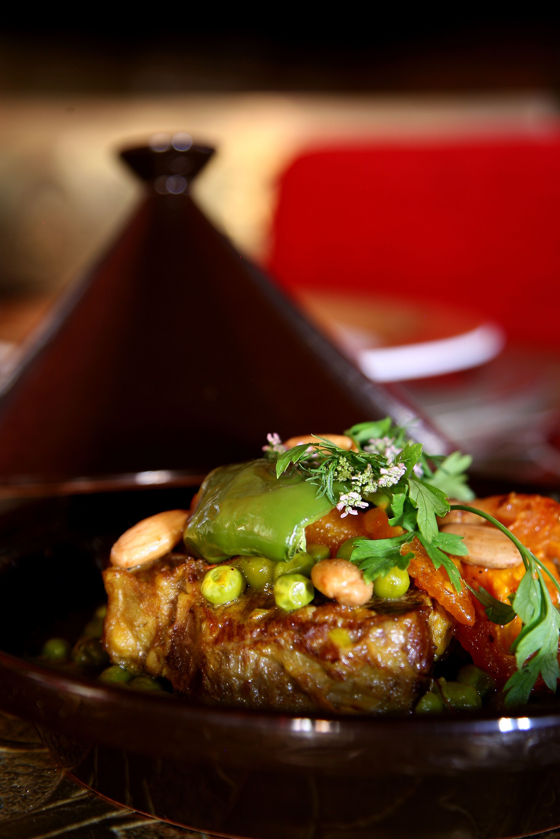 Un plato con carne, guisantes verdes y almendras, adornado con hierbas.