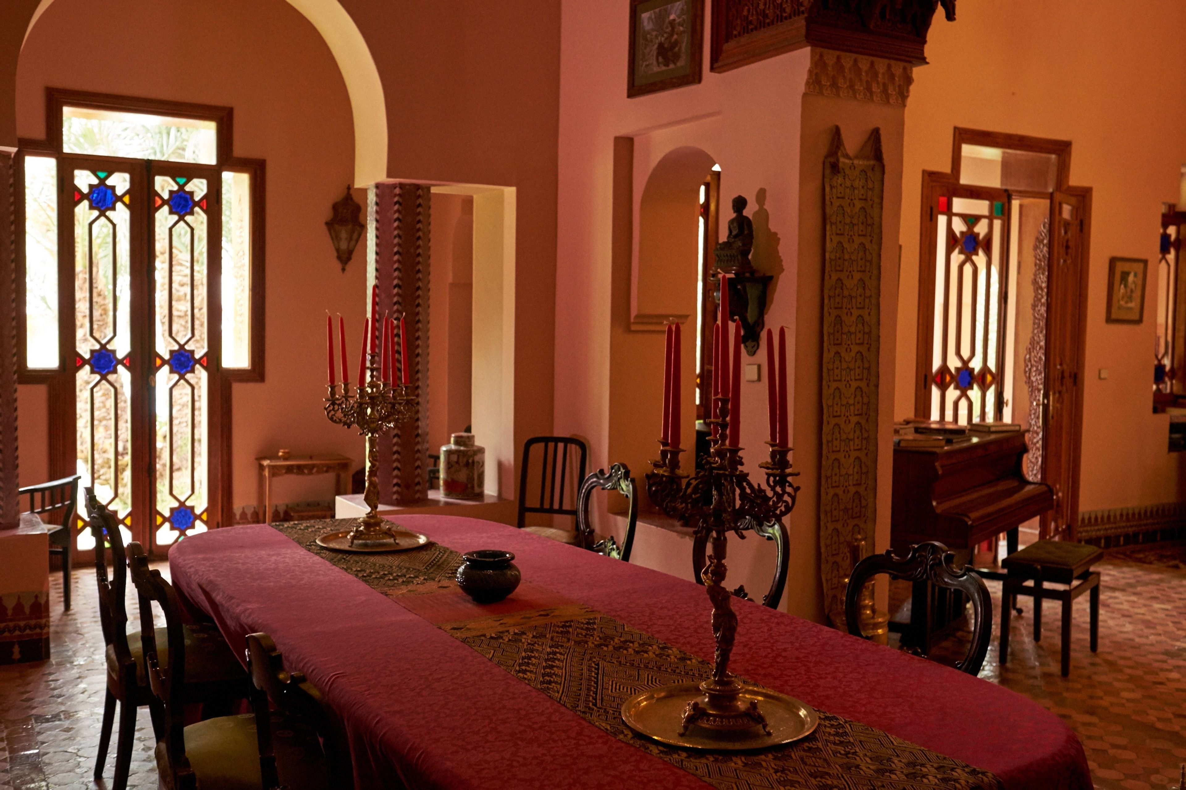 A dining area with a long table, chairs, a chandelier, and a piano.