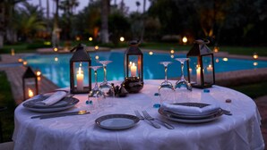 Un espace de restauration en plein air avec une table dressée pour deux personnes, agrémenté de bougies, de verres à vin et offrant une vue sur la piscine.