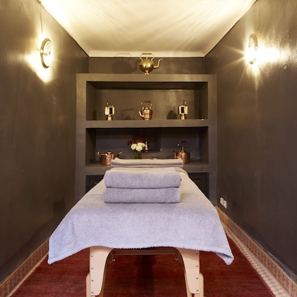 A room with a massage table, shelves with decorative items, and wall sconces.