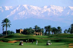 Un campo de golf con un club de campo, palmeras y montañas nevadas al fondo.