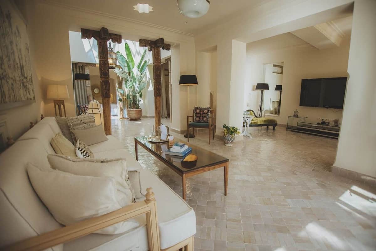 A spacious living room with a sofa, coffee table, and a TV. There is a large plant and a wooden column in the center.