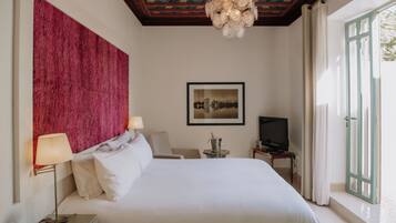 Quarto de hotel com uma cama grande, televisão, escrivaninha com luminária e vista para o exterior pela janela.