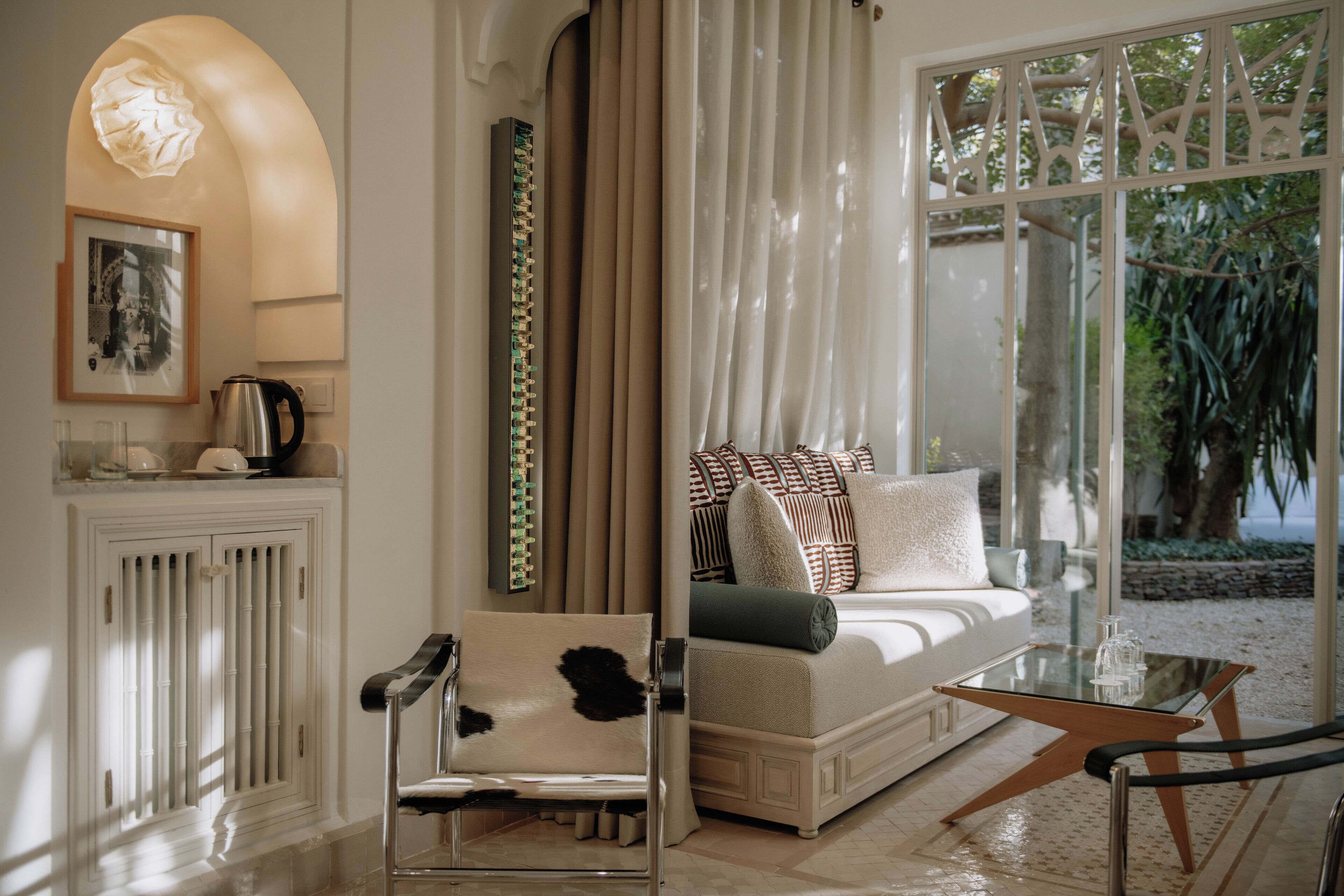A modern living room with a sofa, a glass coffee table, and a chair. There is a fireplace, a picture frame, and a view of the outdoors.