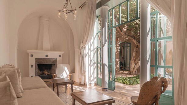 A spacious living room with a fireplace, a large window, and a view of an outdoor area. - Les Deux Tours (Marrakech)