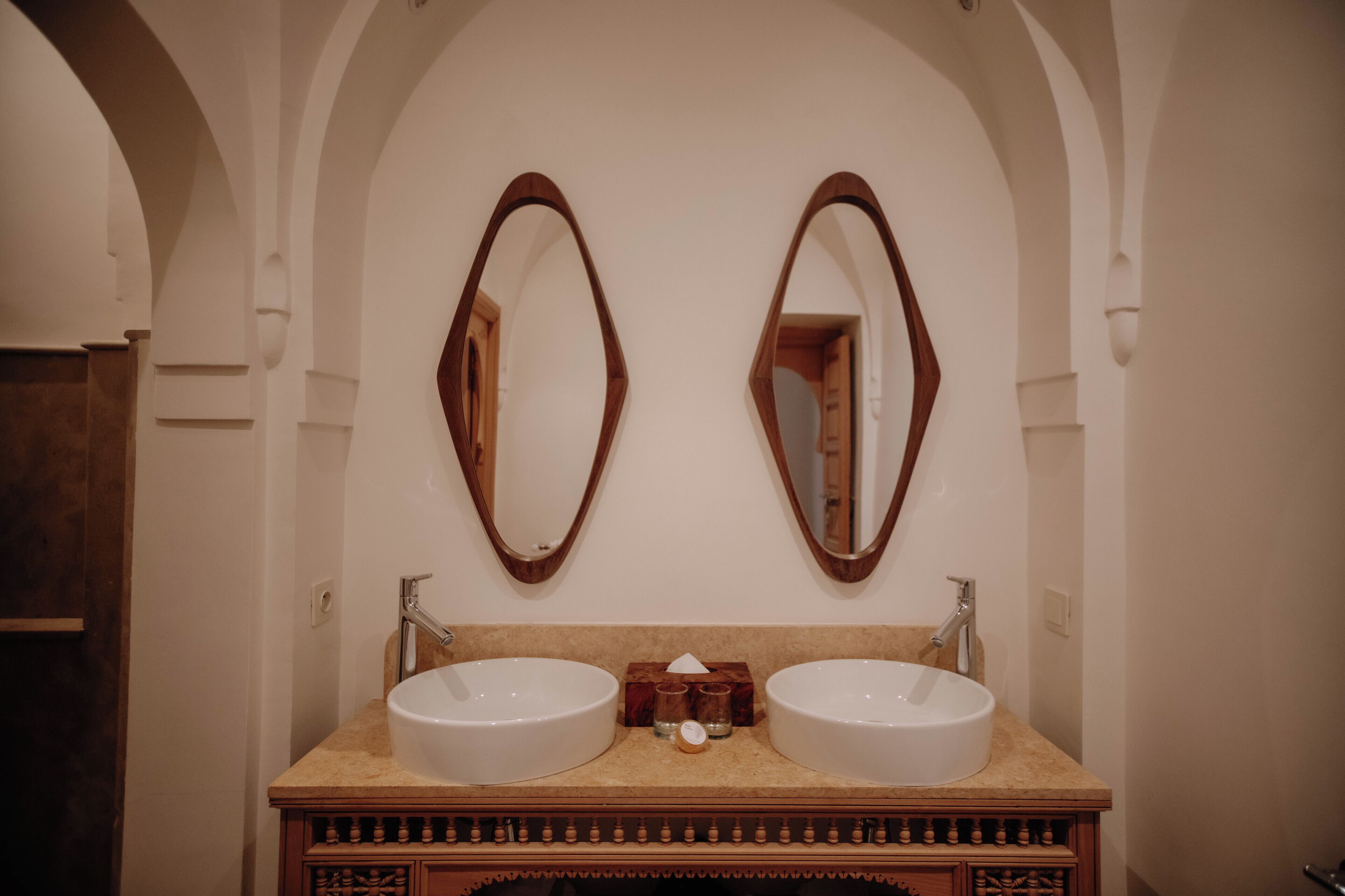 Une salle de bain avec deux lavabos, un meuble-lavabo en bois et des alcôves en forme d’arc.