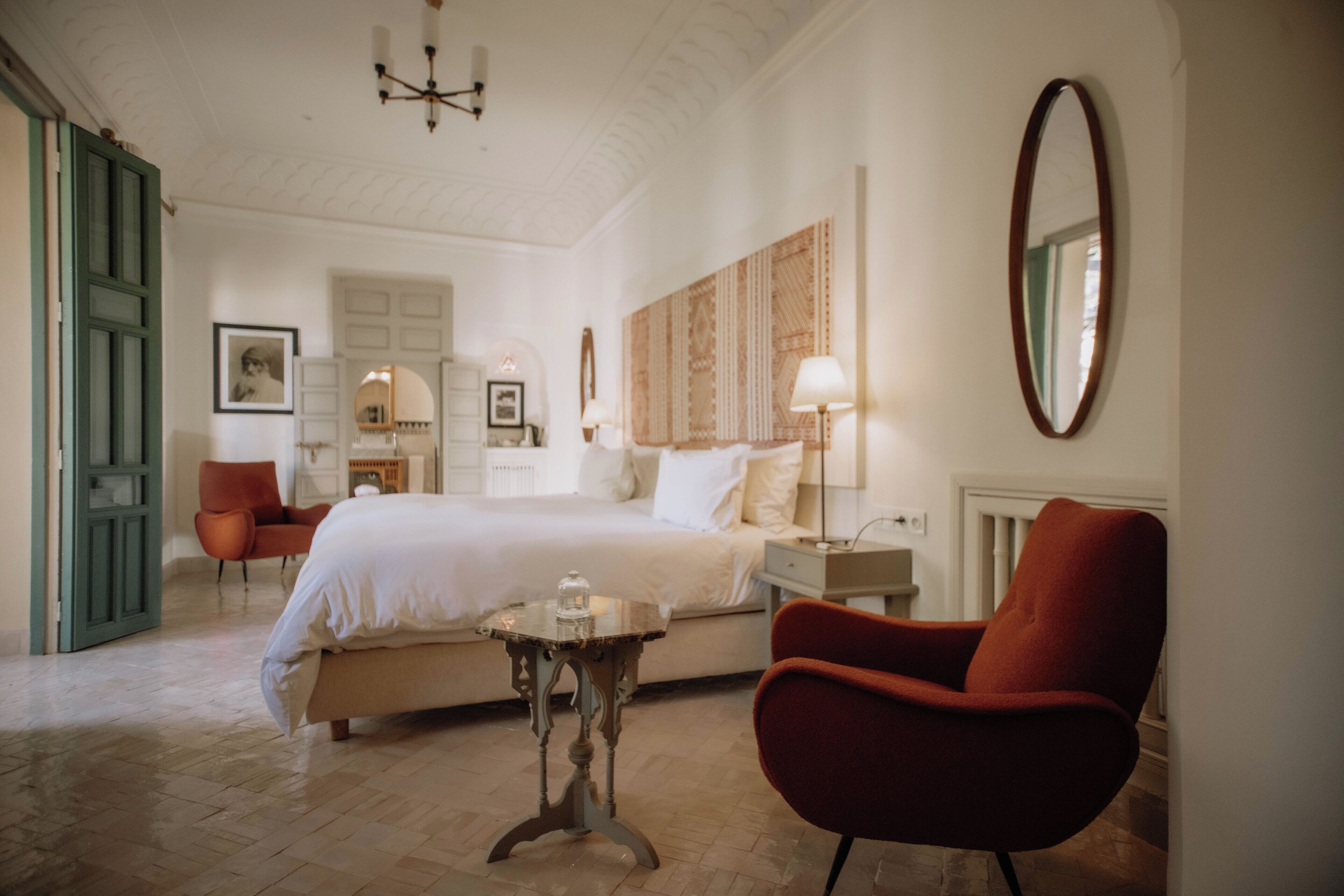 Une chambre d’hôtel avec un lit, un fauteuil rouge, une petite table et un miroir au mur.