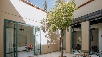 Habitación de hotel con cama, una mesita y una silla. Hay un árbol en el centro de la habitación.