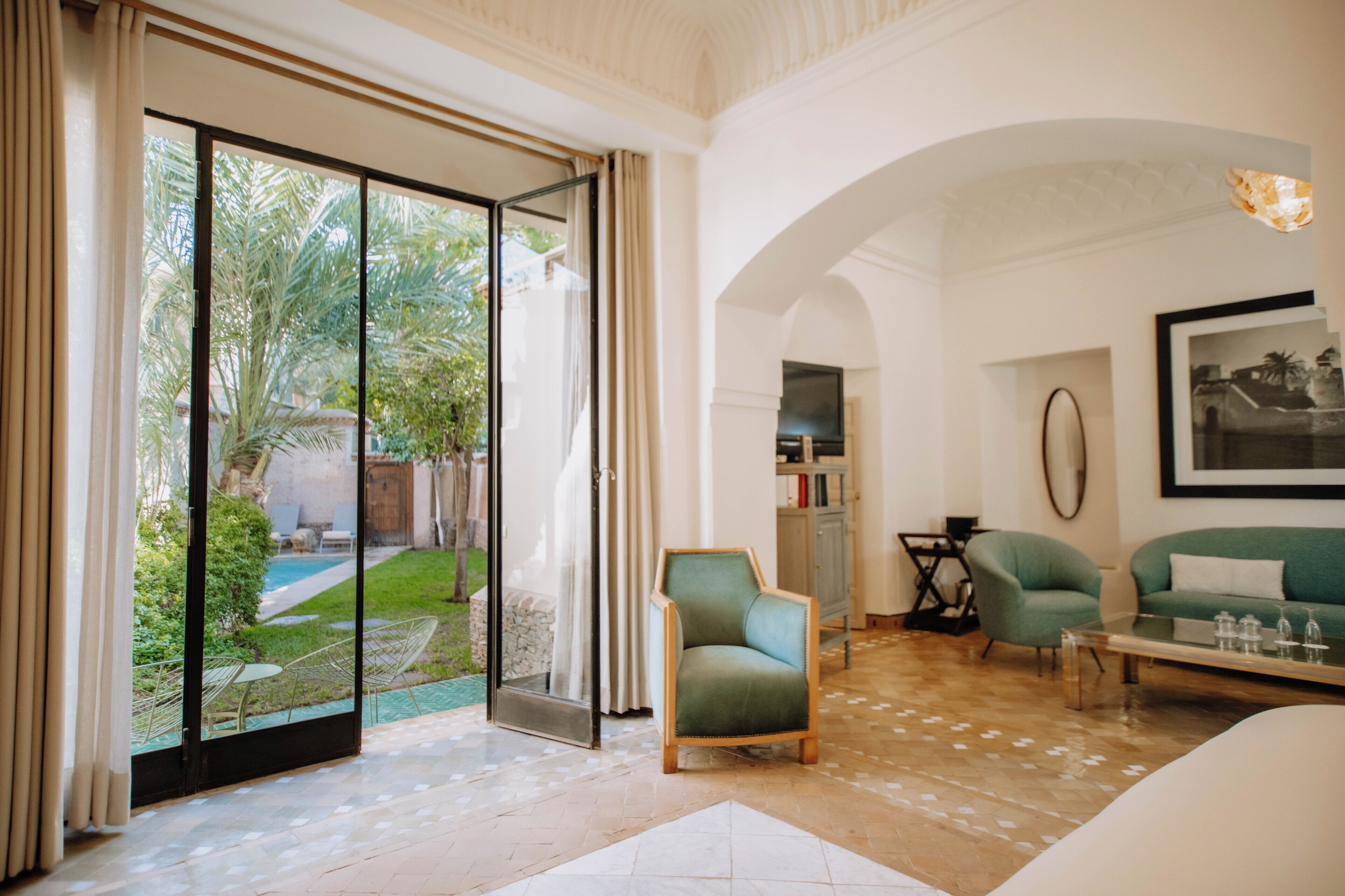 Amplia sala de estar con puerta corrediza de vidrio que da a un jardín, un sillón verde, un sofá color turquesa y una mesa de centro.