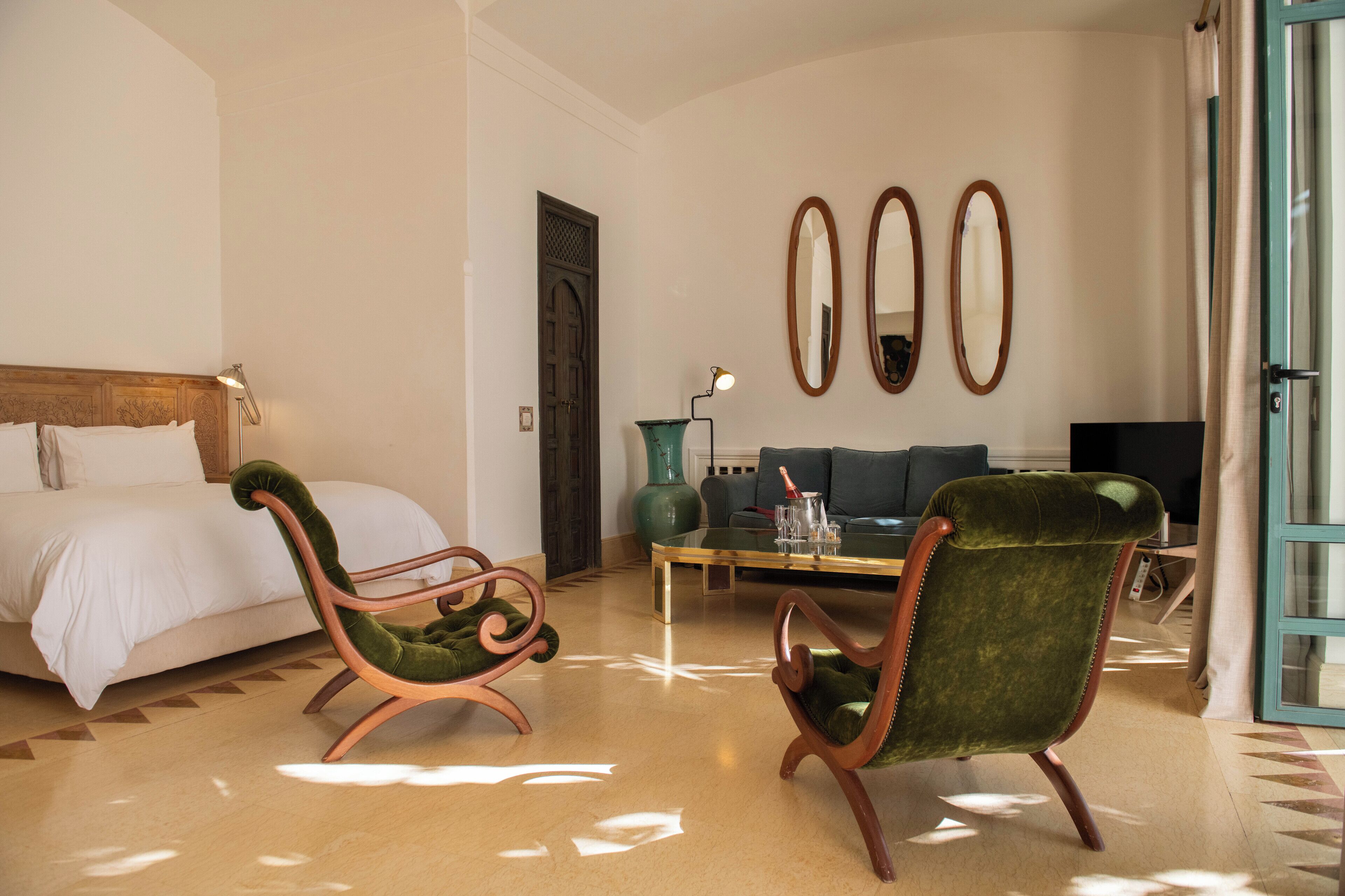 Habitación de hotel con una cama, dos sillones tapizados en verde, un sofá, una mesa de centro y una televisión.