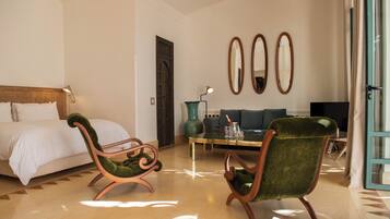 Habitación de hotel con una cama, dos sillones tapizados en verde, un sofá, una mesa de centro y una televisión.