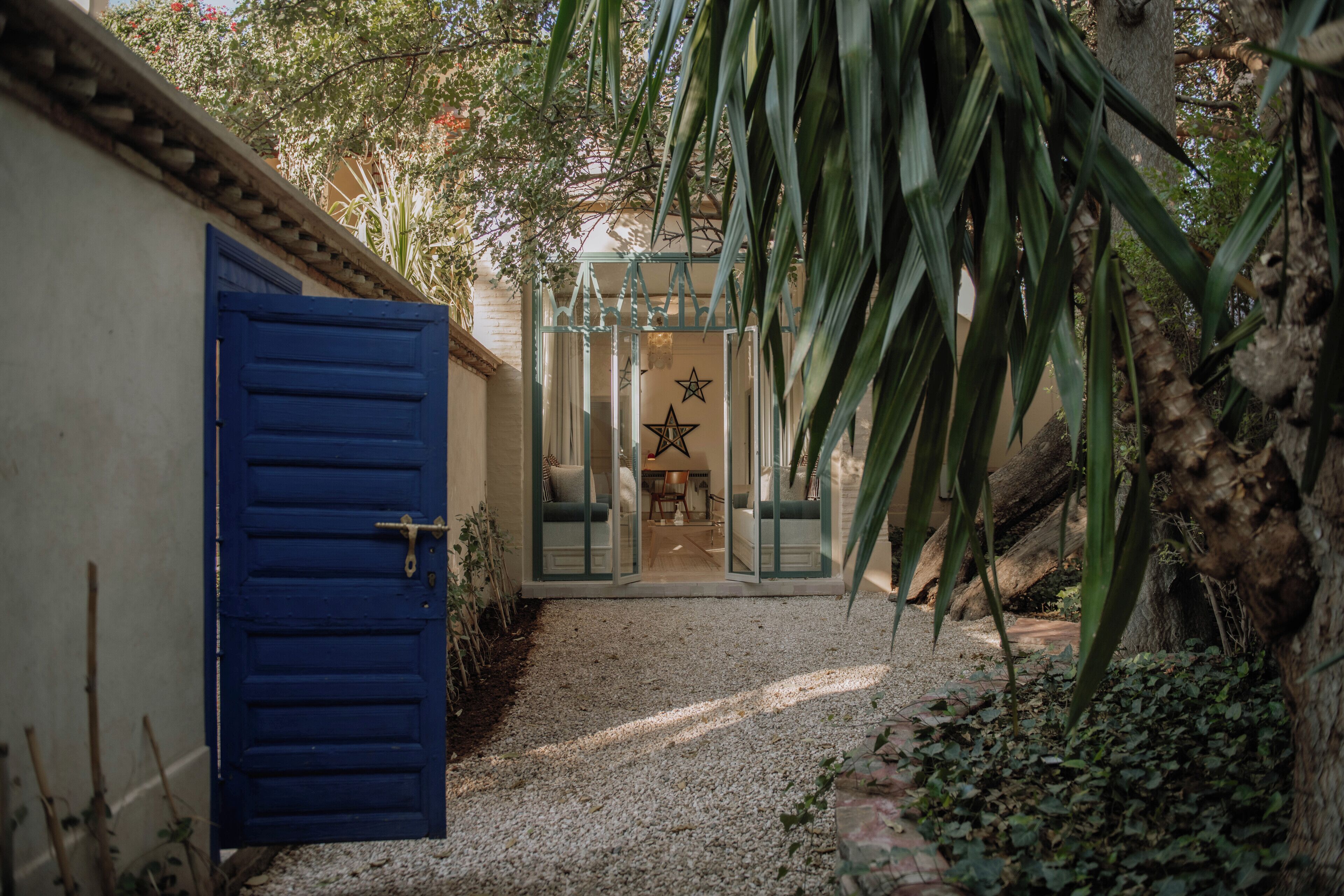 A pathway leading to a door with a star decoration, surrounded by greenery and a gravel path.