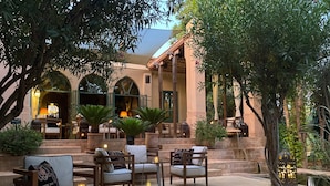 An outdoor seating area with stone tables and chairs, surrounded by greenery and architectural features. - Les Deux Tours (Marrakech)