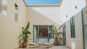 A sunlit indoor pool area with lounge chairs, potted plants, and a view of the interior through glass doors. - Les Deux Tours (Marrakech)