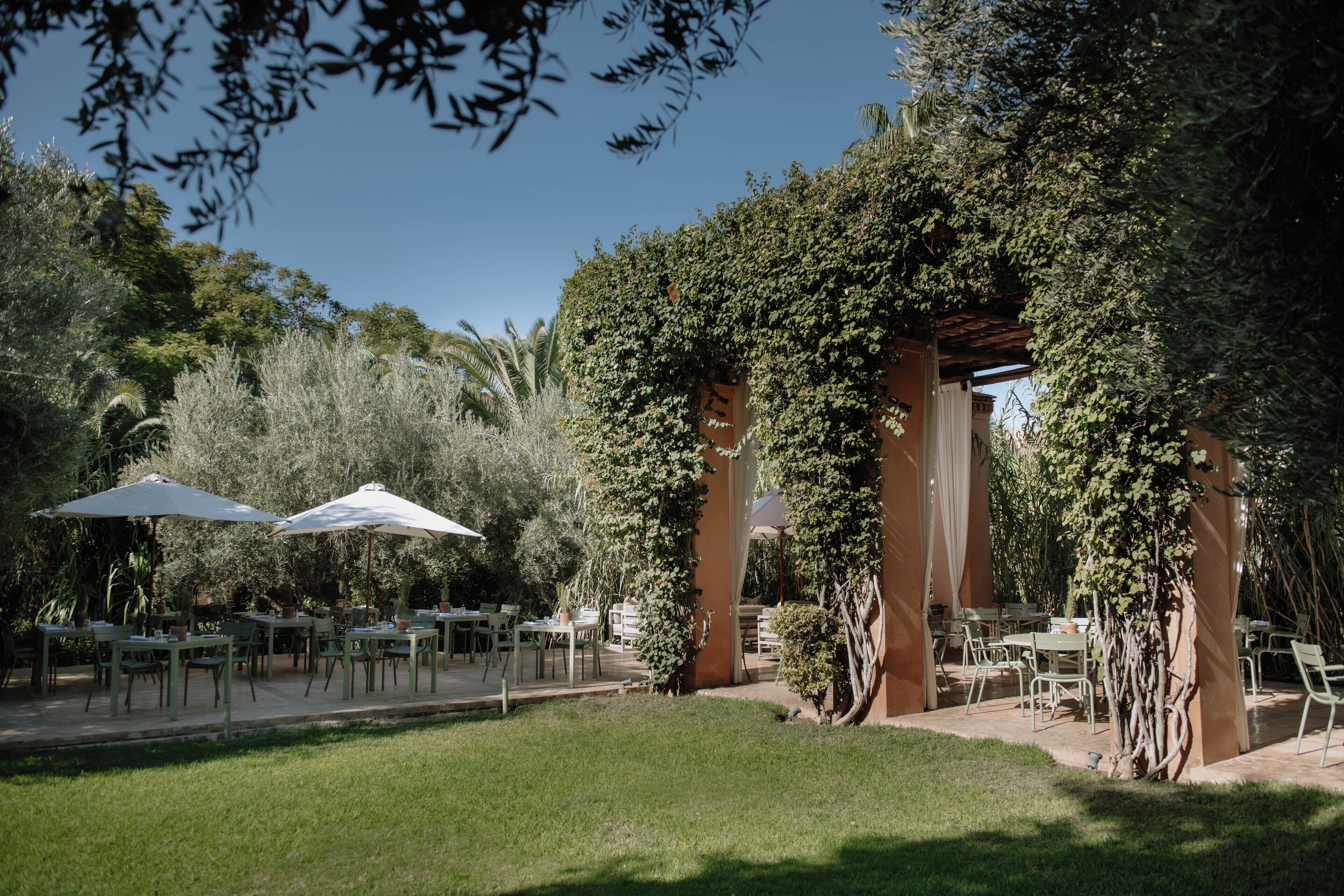Zona d'aigües amunt per dinar amb taules i caires, envoltada de vegetació i coberta per una pèrgola.