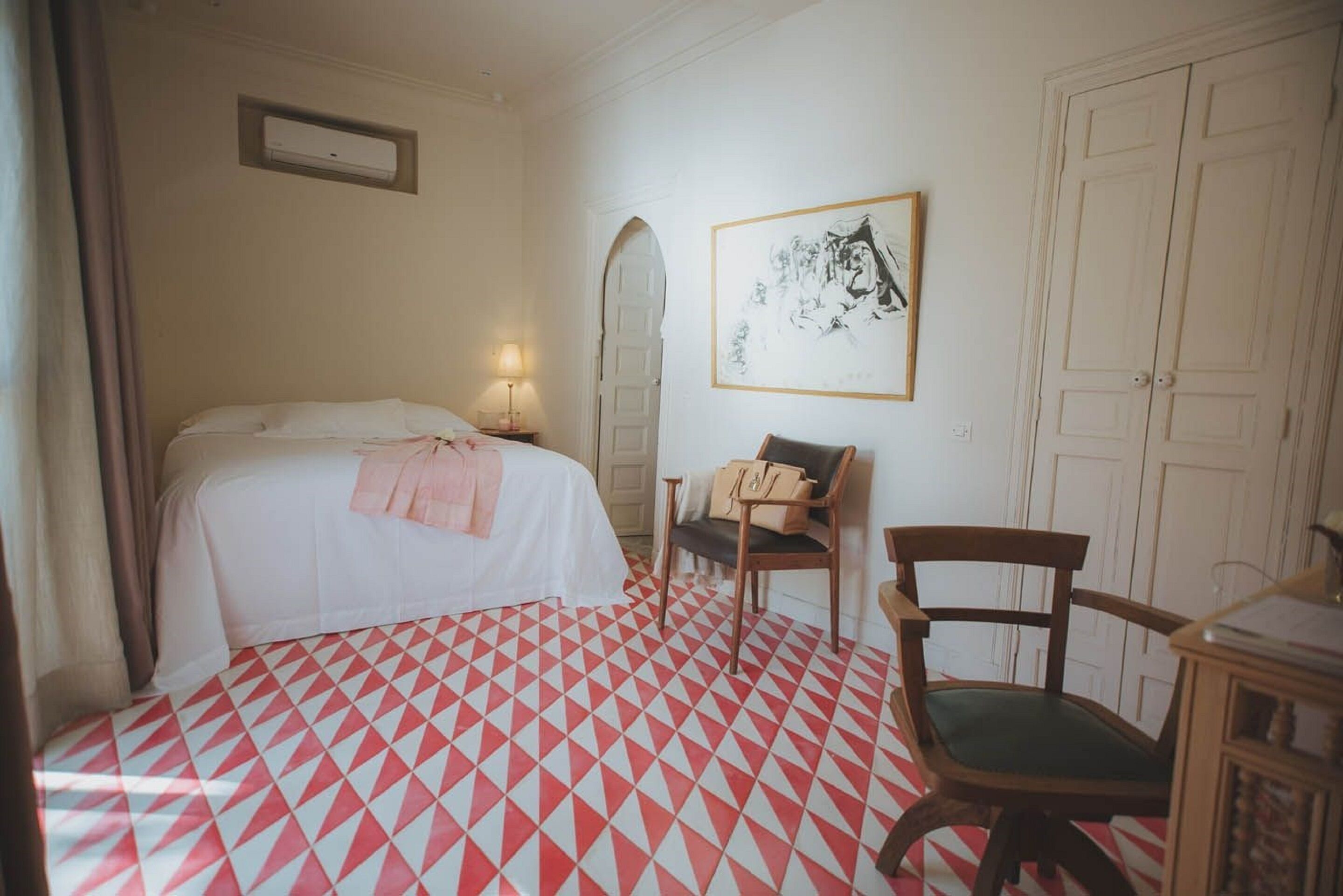 A hotel room with a bed, a chair, a desk, a mirror, and a painting on the wall.