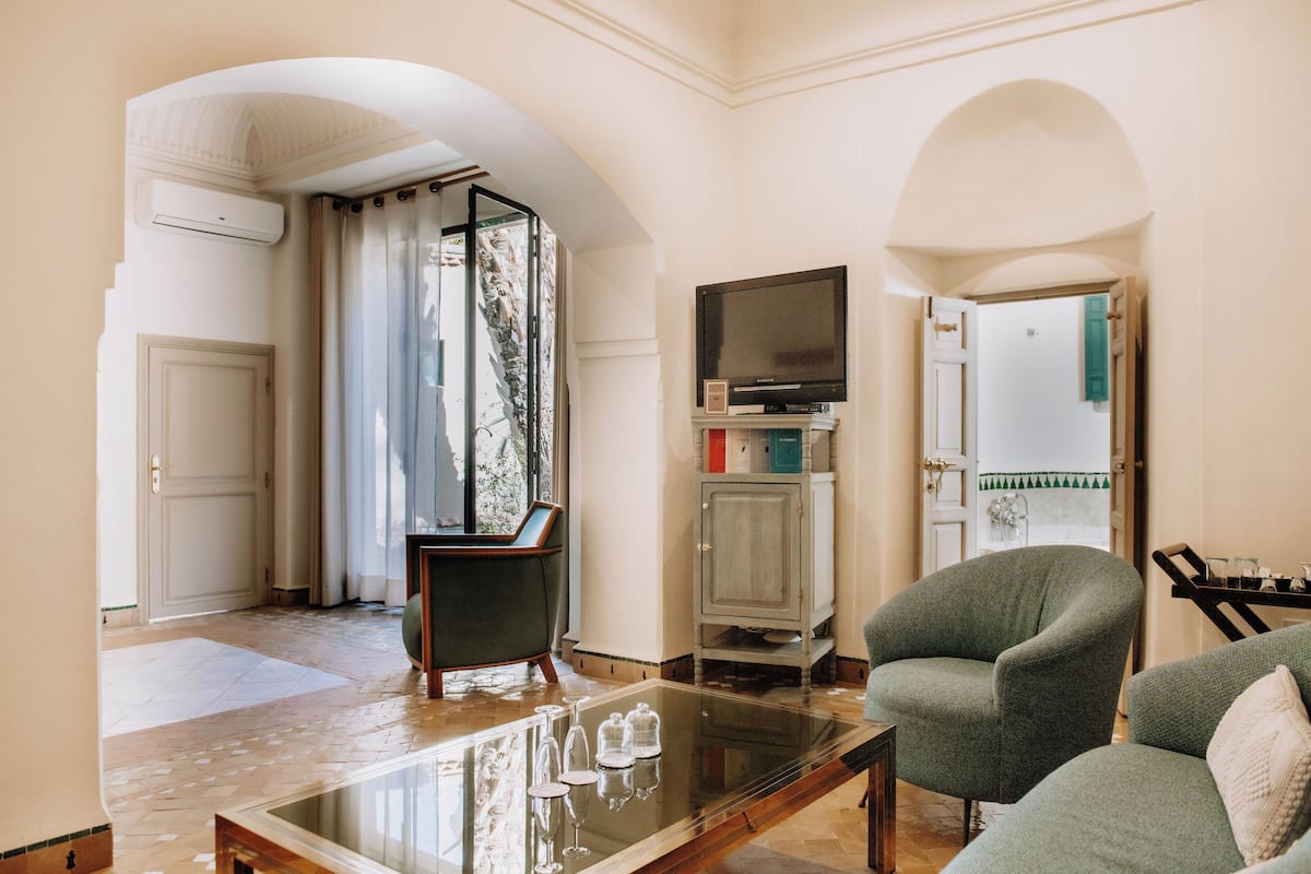 A living room with a glass coffee table, two armchairs, a television, and a cabinet.