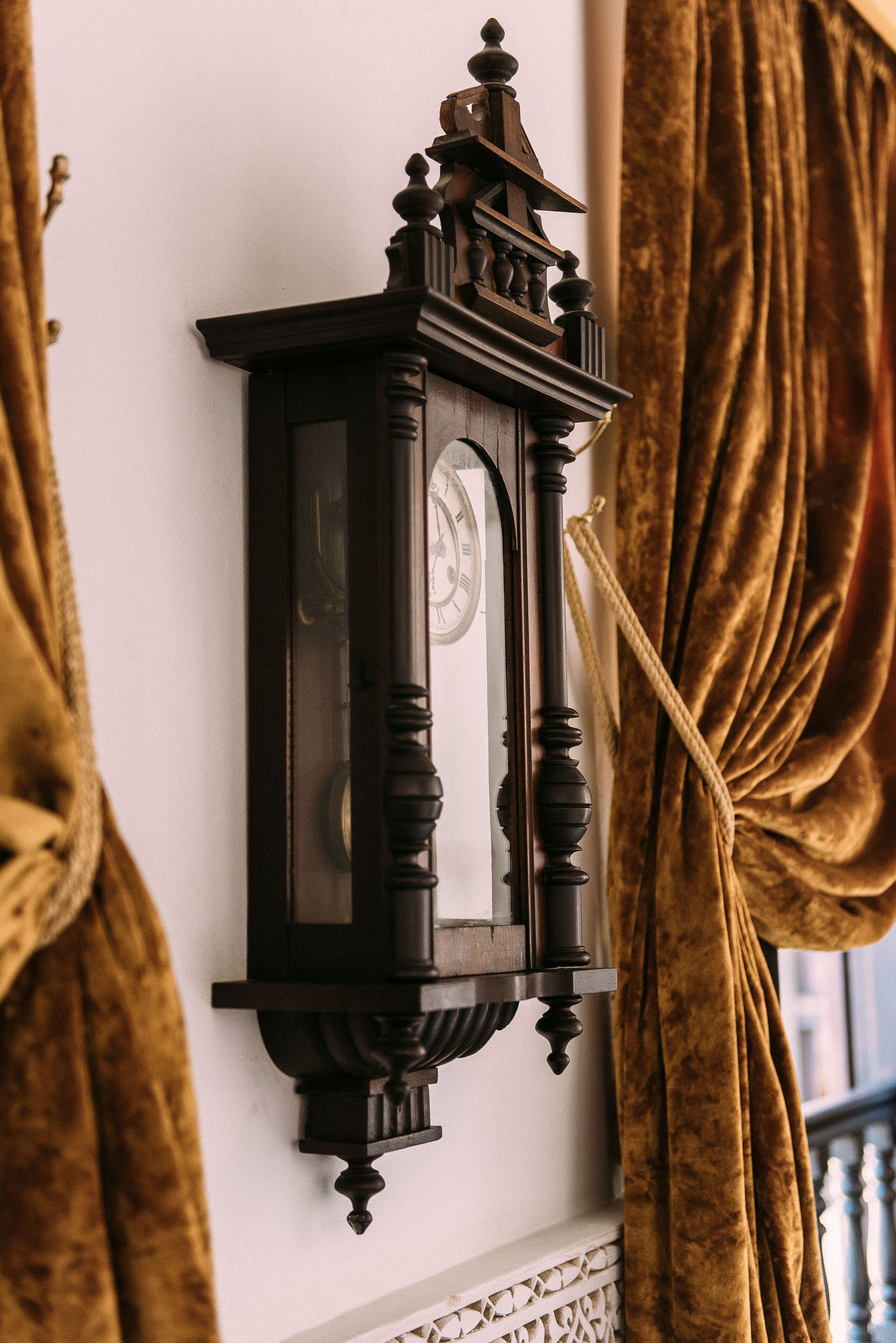 A wall-mounted clock with a classic design, a rope tied around it, and a curtain partially covering it.