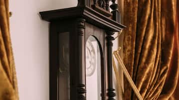 A wall-mounted clock with a classic design, a rope tied around it, and a curtain partially covering it.