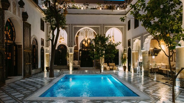 A swimming pool with tiled flooring, surrounded by arches and columns, and furnished seating areas. - Riad Maison Bleue And Spa (Fes)