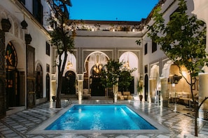 A swimming pool with tiled flooring, surrounded by arches and columns, and furnished seating areas.
