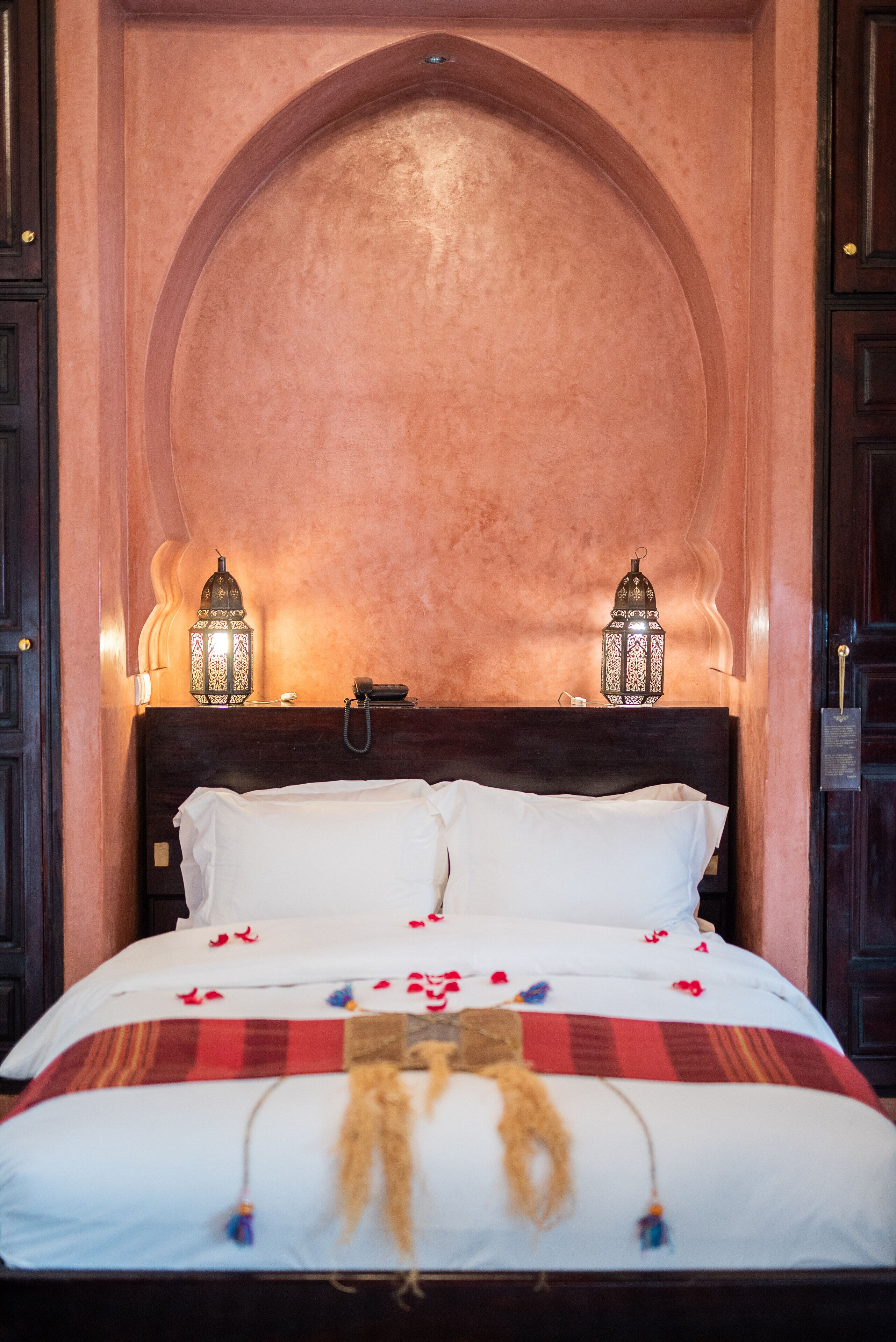 A bed with white linens, two wall-mounted lanterns, and a decorative headboard.