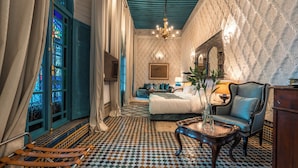 A room with a bed, a chair, a table, a mirror, and a patterned floor. - Riad Maison Bleue And Spa (Fes)