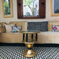 Un sofá con cojines estampados, una mesita de bronce y un suelo a cuadros.